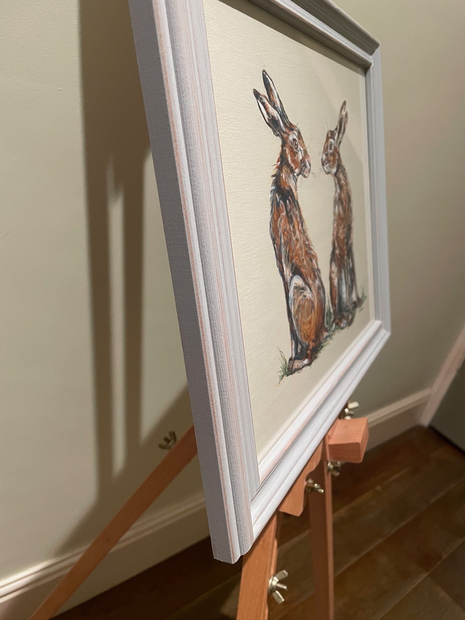 This painting features two hares in a heart shaped composition.   These characterful hares have been spied before they leap across the countryside meadow.