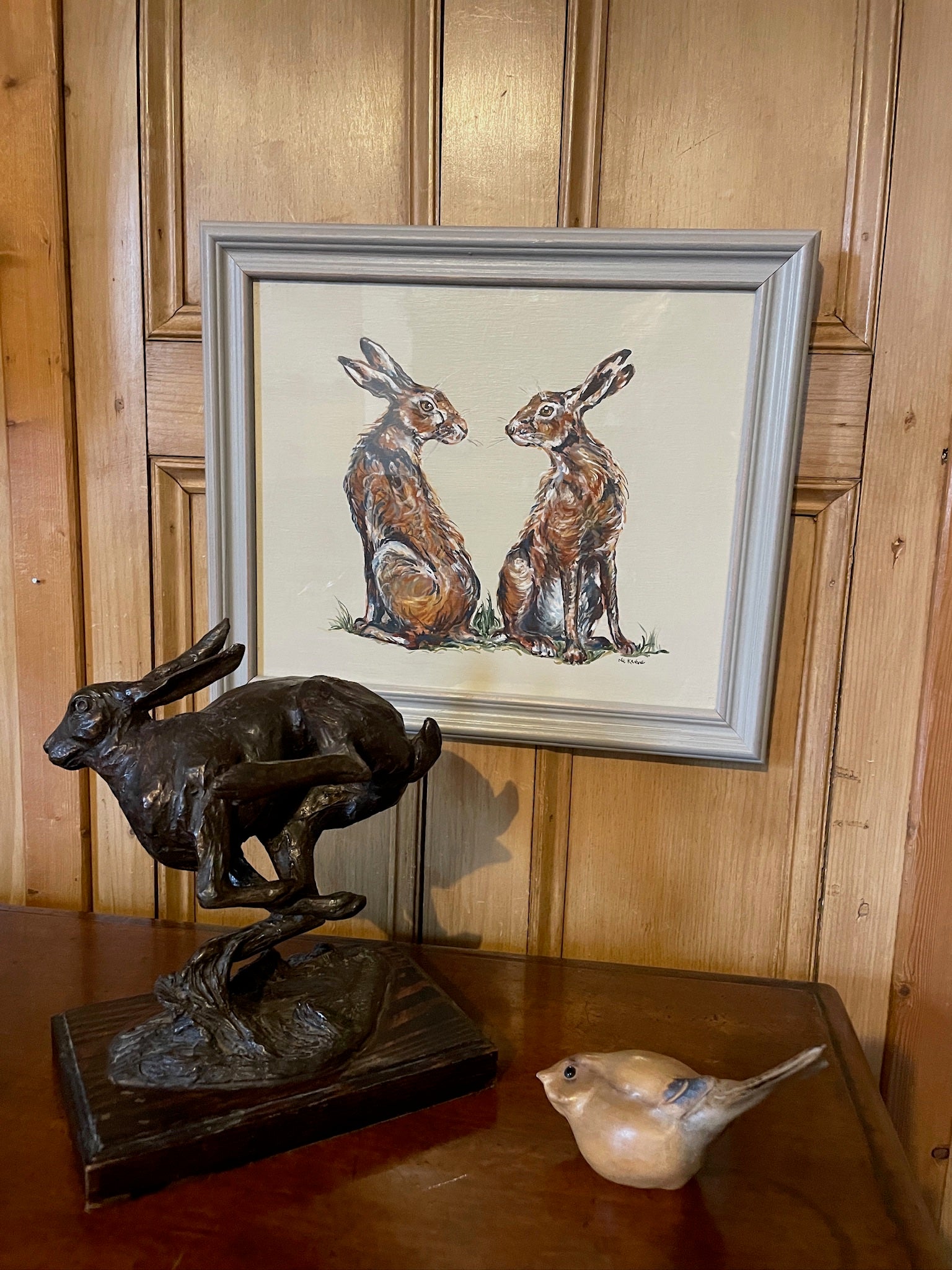 This painting features two hares in a heart shaped composition.   These characterful hares have been spied before they leap across the countryside meadow.